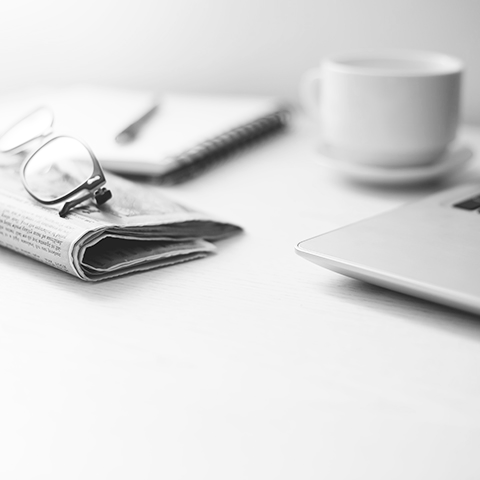 glasses on top of newspaper with cup of coffee and laptop